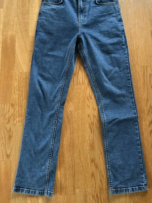 Blå raka Grunt jeans i klassisk modell - Ett par blå jeans med rak passform och hög midja. Jeansen har fem fickor och synliga sömmar i kontrastfärg. Tillverkade i klassiskt denimtyg som ger en tidlös look. Perfekta för dig som gillar enkel och stilren stil.