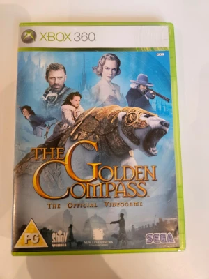 The Golden Compass Xbox 360 spel - The Golden Compass är ett actionäventyrsspel till Xbox 360, baserat på filmen och boken. Omslaget har en isbjörn i rustning och flera karaktärer mot en blå bakgrund. Spelet är i plastfodral med tydlig Xbox 360-märkning och SEGA-logga.