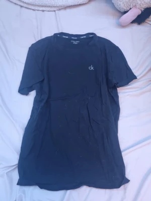 Svart Calvin Klein t-shirt - Snygg svart t-shirt från Calvin Klein med diskret 'ck'-logga på bröstet. Klassisk rund halsringning och korta ärmar. Tillverkad i mjukt bomullsmaterial som känns skönt mot huden. Perfekt för en clean och stilren look.