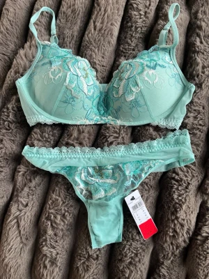 Mintgrönt spetsset från Intimissimi - Snyggt underklädesset i mintgrönt från Intimissimi med broderade blommor i vitt och turkost. Setet består av en vadderad bh med justerbara axelband och matchande trosa med spetsdetaljer. Materialet är tunt och genomskinligt med vacker spetskant.