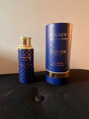 Legacy Royal Collection Maison Asrar parfym - Exklusiv parfym från Maison Asrar, Legacy Royal Collection. Flaskan är mörkblå med guldiga detaljer och ett elegant geometriskt mönster. Kommer i en matchande blå och guldig tubformad förpackning. Perfekt för dig som gillar lyxiga och unika dofter.