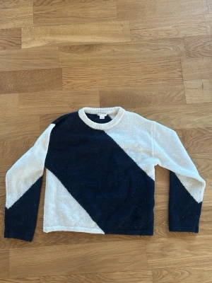 Stickad tröja från Gina Tricot - Cool stickad tröja från Gina Tricot med diagonal färgblock i mörkblått och vitt. Tröjan har rund halsringning och långa ärmar, perfekt för att ge din outfit en modern touch. Materialet är mjukt och skönt, och designen är riktigt trendig.