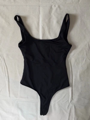 Svart basic baddräkt med breda axelband - En stilren svart body med breda axelband och rundad urringning både fram och bak. Modellen är enkel och tight. Använd 1 gång.