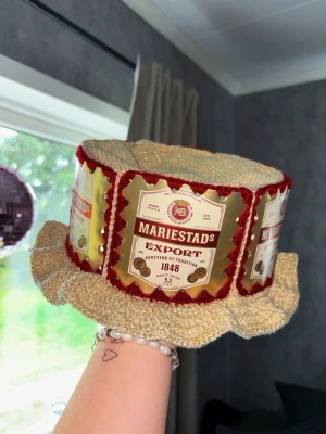 Virkad Mariestad ölhatt 🍺  - Virkad Mariestad ölhatt – handgjord & unik 🍺 En rolig och charmig ölhatt inspirerad av Mariestad, perfekt för fest, kräftskiva, midsommar, student eller som en kul present till ölälskaren! ✨Passar lika bra som accessoar till festen som dekor i hemmet eller barhörnan!! 🍻