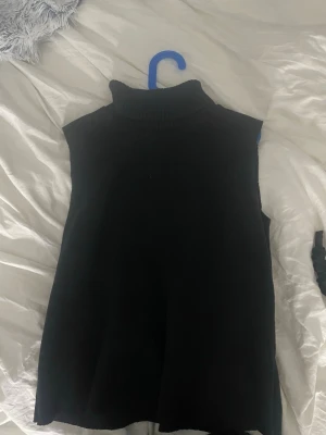 Svart ärmlös polotröja - Svart stickad ärmlös polotröja med hög krage. Perfekt att styla över en skjorta eller bära som den är. Mjuk och skön känsla, rak passform och enkel design som funkar till många outfits.