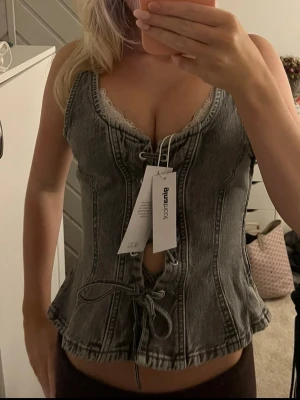 topp med snörning - Trendigt grå korsettopp i denim från Gina Tricot med snygg snörning framtill. Toppen har markerade sömmar, v-ringning och är ärmlös. säljer denna helt nya jeanstopp från Gina Tricot med knyten/snörningar. Prislapp kvar, storlek XS. Man kan ha den åt båda hållen! Nypris 400kr 