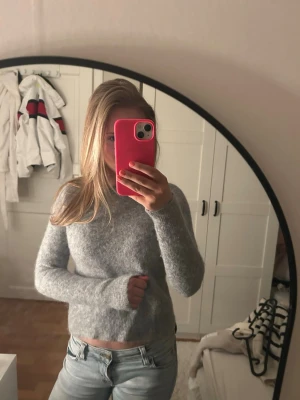 Grå stickad tröja i mjuk ullmix - Mysig grå stickad tröja med rund hals och långa ärmar. Tröjan har en enkel, klassisk design och är tillverkad i ett mjukt material som känns skönt mot huden. Perfekt att matcha med jeans för en avslappnad look.