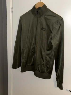 Tröja  EA7 emporio armani  - Köpt för 1000kr på NK. Stilren grön zip- från EA7 Emporio Armani med hög krage och diskret logga på bröstet. Jackan har långa ärmar, ribbade muddar och två fickor framtill. Perfekt för dig som gillar sportig och clean stil.