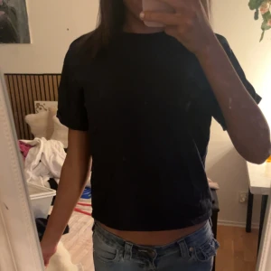 Marinblå croppad topp från Gina Tricot - En enkel och stilren svart croppad topp från Gina Tricot. Toppen har korta ärmar och rund halsringning. Perfekt att matcha med höga jeans eller kjol för en clean look.