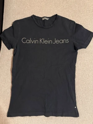 Svart Calvin Klein Jeans t-shirt XS - Svart t-shirt från Calvin Klein Jeans med klassisk rund hals och stort tryck över bröstet. T-shirten är kortärmad och har en slim passform. Perfekt för en clean och stilren look.