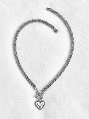 Silverfärgat halsband med hjärthänge - Snyggt halsband i silverfärgad metall med en grov kedja och ett hjärtformat hänge. Halsbandet har ett dekorativt toggle-lås framtill som ger en trendig touch. Hjärtat har en fin kantdetalj som gör smycket extra unikt. Perfekt accessoar för att lyfta din outfit.