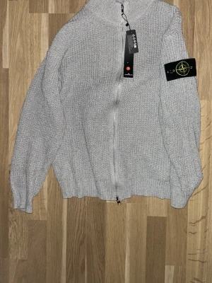 Ljusgrå stickad ziptröja Stone Island - Säljer en ljusgrå stickad ziptröja från Stone Island med ikonisk patch på ärmen. Tröjan är som en quarter zip fast med lång zip