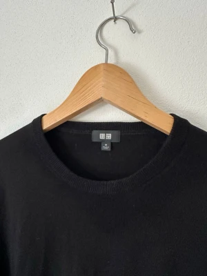 Svart stickad tröja från Uniqlo - Klassisk svart stickad tröja från Uniqlo med rund halsringning och långa ärmar. Enkel och stilren design som passar till det mesta. Tröjan är tillverkad i ett mjukt material och har ribbade muddar vid ärmslut och nederkant. 8B11