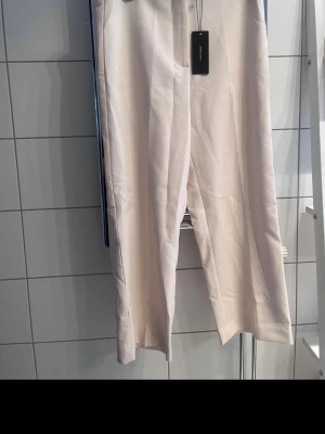 Vida vita kostymbyxor Weekday - Stilrena kostymbyxor från Weekday i en fräsch beigevit färg. Byxorna har en rak och vid passform med pressveck framtill och diskreta fickor i sidorna. Perfekta för en clean och modern look.