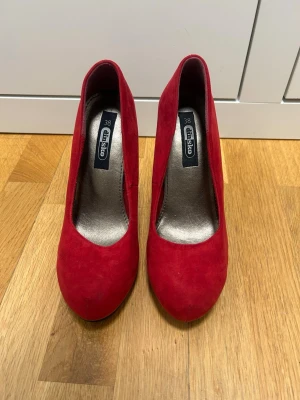 Röda pumps från Din Sko - Snygga röda pumps från Din Sko i storlek 38. Skorna har en klassisk rund tå och hög klack. Ovandelen är i röd mockaimitation som ger en lyxig känsla. Perfekta för att lyfta vilken outfit som helst.