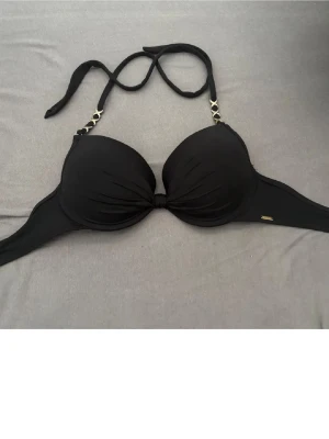 Svart bikiniöverdel push up - Snygg svart bikiniöverdel med vadderade kupor och guldfärgade kedjedetaljer vid axelbanden. Knyt i nacken för justerbar passform. Perfekt för strandhäng eller poolparty.