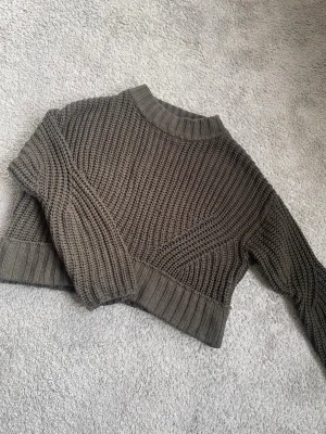 Skogsgrön stickad tröja - Säljer en stickad tröja i skogsgrön färg med grov ribbad struktur. Tröjan har lång ärm, bred ribbad mudd vid ärmslut och nederkant samt en högre rund halsringning. Perfekt för lager på lager och en chill look.