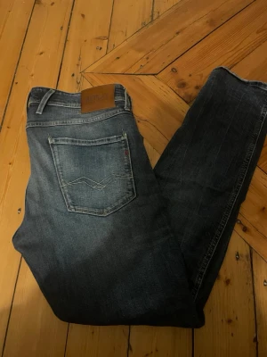 Replay Anbass - Snygga mörkblå jeans från Replay med klassisk femficksdesign och raka ben. Jeansen har en diskret tvättad look och detaljer som läderpatch med logga bak i midjan. Tillverkade i slitstark denim med coola sömmar på bakfickan.