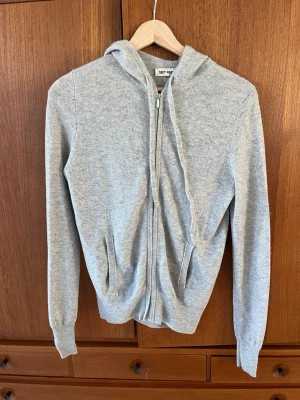 Ljusgrå hoodie med dragkedja från Soft Goat storlek xs - Mjuk och stilren ljusgrå hoodie från Soft Goat i kashmir / cashmere . Hoodien har dragkedja framtill, två fickor och en klassisk huva. Perfekt för en avslappnad look och enkel att matcha med andra plagg. I fint använt skick.