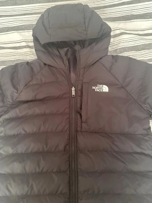 Svart jacka från The North Face - Snygg svart jacka från The North Face med huva och dragkedja framtill. Jackan har quiltad design och en diskret bröstficka med logga på vänster sida. Perfekt för kalla vinterdagar och riktigt skön att bära. Om du vill ha mer information skriv till mig på dm!
