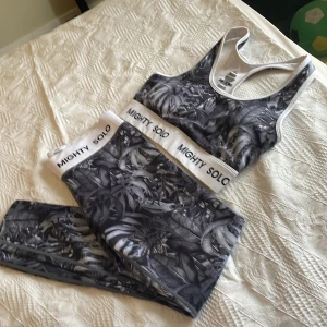 Mönstrat träningsset från Mighty Solo - Snyggt träningsset från Mighty Solo med svartvitt tropiskt mönster. Setet består av sport-bh och tights med bred resår och logga. Materialet är stretchigt och består av 73% polyester och 27% spandex, vilket ger bra passform och komfort under träningen.Knappt använda alls.