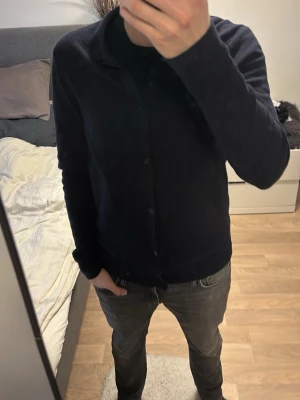 Mörkblå cardigan från Weekday - Säljer en stilren mörkblå cardigan med knäppning framtill och klassisk krage. Tröjan har en mjuk och lite tunnare struktur, perfekt att slänga över en t-shirt. Passar dig som gillar minimalistisk och clean stil. Passar M och L minst lika bra