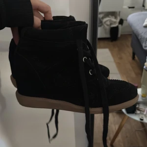 Svarta höga sneakers med kilklack - Snygga svarta sneakers med kilklack och sula i beige. Skorna har högt skaft, snörning framtill och är tillverkade i mockaliknande material. Storlek 36, så snygga!