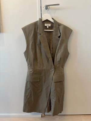 Grön ärmlös linneklänning från & other stories - Stilren grön klänning från & Other storie i linne med ärmlös design och klassisk krage. Klänningen har en knapp framtill, två fickor 