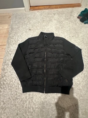 Svart cardigan från Moncler - Snygg svart dunväst från Moncler med quiltad framsida och släta ärmar. Västen har dragkedja framtill, ståkrage och diskret Moncler-logga på ärmen. Perfekt för lager-på-lager och håller dig varm med stil. Storlek 5