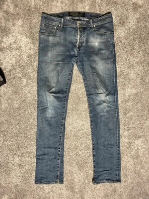 Jacob cohën limited edition jeans  - Säljer ett par klassiska blå slim fit jeans med fem fickor och knappgylf. Jeansen har en snygg tvätt med lätt slitning och kontrastsömmar. Perfekta för dig som gillar en smalare passform och tidlös stil.