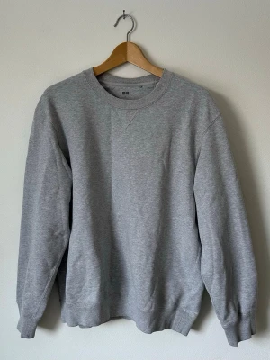 Grå sweatshirt från Uniqlo - Klassisk grå sweatshirt från Uniqlo i mjuk bomullsblandning. Tröjan har rund halsringning, ribbade muddar vid ärmslut och nederkant samt en relaxed passform. Perfekt basplagg för en enkel och clean stil. 8A14
