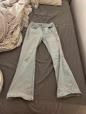 Ljusblå utsvängda jeans - Säljer ett par ljusblå jeans med utsvängda ben och klassisk femficksmodell. Jeansen har medelhög midja och är tillverkade i mjukt denimtyg som är stretchigt. Tyvärr har dom en fläck och är lite sönder, men annars sitter dom jätte fint på en! W29 L32