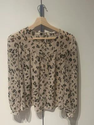 Beige blus med leopardmönster - Snygg beige blus med leopardmönster och transparent tyg. Blusen har rund halsringning och långa ärmar med resår vid ärmslut. 