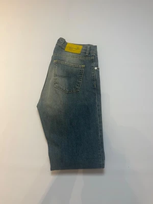 Blå Jacob Cohen jenans W33 - Snygga blå jeans från Jacob cohen med raka ben och klassisk femficksdesign. Jeansen har en ljus tvätt och en gul patch med logga baktill i midjan. Perfekta för en avslappnad och trendig stil. Jeansen har storlek W33