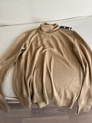 Beige polotröja från BOSS - Snygg beige stickad polotröja från BOSS med klassisk passform och lång ärm. Tröjan har en mjuk och tunn stickning som gör den perfekt för lager-på-lager och en stilren look. Perfekt för dig som gillar minimalistisk stil.