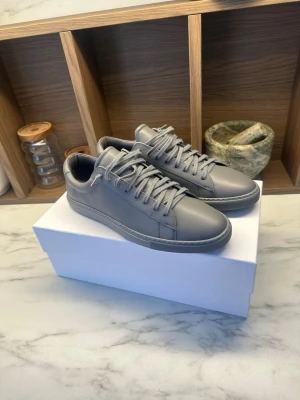 Grå Oliver cabel  sneakers i grå läder - Stilrena grå sneakers från Oliver cabel i slätt grått  läder med matchande grå snörning och diskret guldtext på sidan. Klassisk låg modell med rund tå och tonad sula, perfekt för en clean och modern look. Nypris 2000kr, använda 0 gånger 