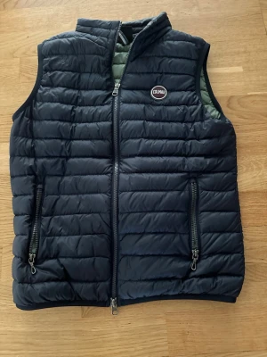 Mörkblå dunväst från Colmar - Snygg mörkblå dunväst från Colmar med quiltad design och två dragkedjefickor framtill. Västen har hög krage och Colmar-logga på bröstet. Perfekt för lager-på-lager och håller dig varm under kyliga dagar. De är storlek 14 år men passar som xs typ