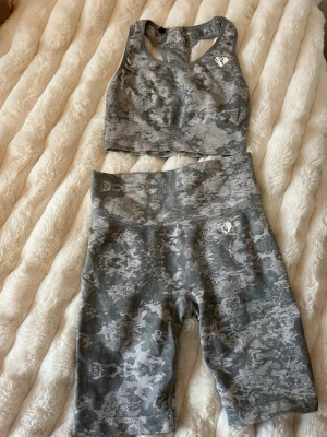 Grått camo träningsset från Gavelo - Snyggt träningsset från Gavelo i grått camomönster. Setet består av en sport-bh med brottarrygg och högmidjade cykelshorts. Båda plaggen har Gavelo-loggan framtill. Materialet är stretchigt och passar perfekt för gym eller träning. Står ingen storlek men passar mig som har xxs, xs och s