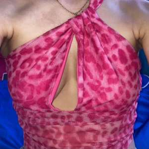 Rosa leopardmönstrad halterneck topp - Trendig rosa halterneck topp med leopardmönster och cut-out detalj framtill. Toppen har en omlottliknande twist vid halsen och är ärmlös. Perfekt för dig som vill sticka ut med färg och mönster.