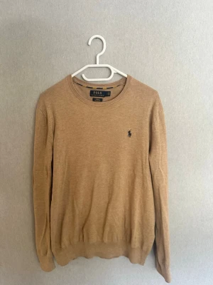 Beige tröja, Polo Ralph Lauren - Snygg beige tröja från Polo Ralph Lauren i slim fit-modell, sitter dock vanligt. Tillverkad av mjuk pima bomull och har rund halsringning samt den klassiska broderade loggan på bröstet. Perfekt för en clean och stilren look. Använd fåtal gånger, schyssta priser vid snabb affär.