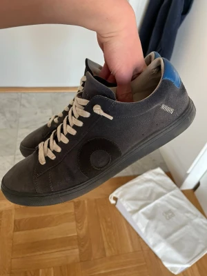 MARINBLÅ OLIVER CABBEL SNEAKEARS - Snygga marinblå sneakers från Oliver cabell med vit sula och vita skosnören. Skorna har en rundad tå, diskret cirkeldetalj på sidan och blå detalj vid hälen. Tillverkade i mocka för en stilren look. Box och dustbag ingår