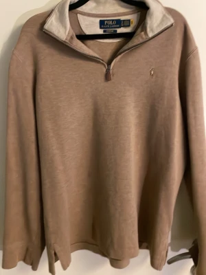 Beige quarterzip från Polo Ralph Lauren - Snygg beige quarterzip-tröja från Polo Ralph Lauren med klassisk broderad logga på bröstet. Tröjan har hög krage med dragkedja och långa ärmar. Perfekt för lager-på-lager och archive men även grish stil. Mjuk bomullsblandning för extra komfort.
