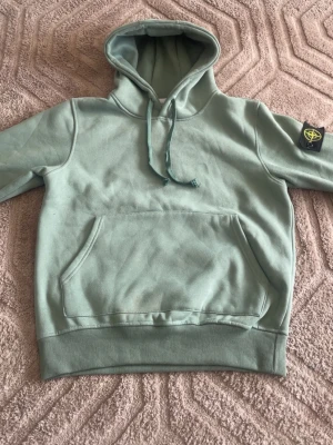Bundle  - Snygg ljusgrön hoodie från Stone Island med klassisk patch på ärmen. Hoodien har känguruficka framtill, dragsko i huvan och ribbade muddar. Perfekt för en avslappnad och trendig stil.