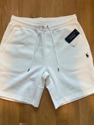 Vita shorts från Polo Ralph Lauren - Snygga vita shorts från Polo Ralph Lauren med dragsko i midjan och klassisk logga broderad på ena benet. Mjukt bomullsmaterial och fickor både fram och bak. Perfekta för en avslappnad och stilren look.