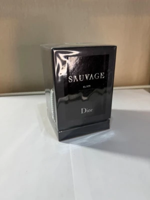 Dior Sauvage Elixir parfym - Dior Sauvage Elixir parfym i en lyxig, svart och silverfärgad rektangulär kartong. Förpackningen är elegant och stilren med tydlig logotyp och text. Perfekt för dig som gillar exklusiva dofter och snygg design.