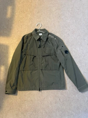 Olivgrön overshirt från C.P. Company - Stilren olivgrön overshirt från C.P. Company med dragkedja framtill, två bröstfickor med dragkedja och klassisk krage. Använd 2 gngr                  Storlek S/M                                                            Perfekt på sommarkvällar samt vår o höst. Nypris 4,700