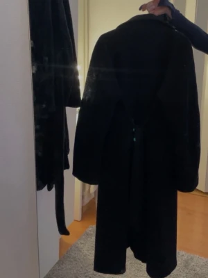 Svart kappa från Gina Tricot - Stilren svart kappa från Gina Tricot i klassisk rak modell. Kappan har krage och är tillverkad i ett mjukt tyg med fodrad insida. Perfekt för kyligare dagar och enkel att matcha med olika outfits.