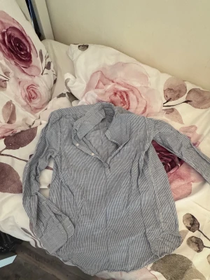 Randig blåvit henley-skjorta - Snygg långärmad henley-skjorta i blåvitt randigt mönster. Skjortan har knappar upptill och är tillverkad i ett lätt och luftigt material, perfekt för en avslappnad stil. Passar dig som gillar klassiska och stilrena plagg.