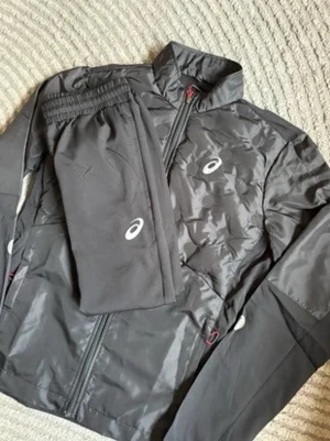 Tracksuit - Snyggt svart träningsset från Asics med jacka och byxor. Setet har dragkedja på jackan, elastisk midja på byxorna och Asics-logga på både jacka och byxor. Materialet är lätt och funkar perfekt för löpning eller gym.