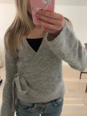 Grå omlottkofta från Gina Tricot - Mysig grå omlottkofta från Gina Tricot. Koftan har knytband i sidan, lång ärm och en mjuk, stickad känsla.